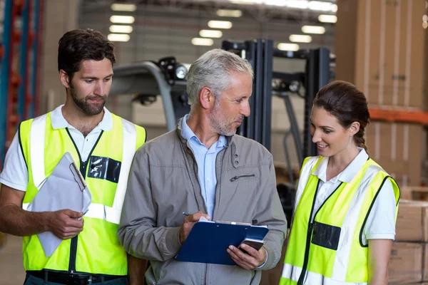 Warehouse manager and workers discussing with clipboard — Stockfoto