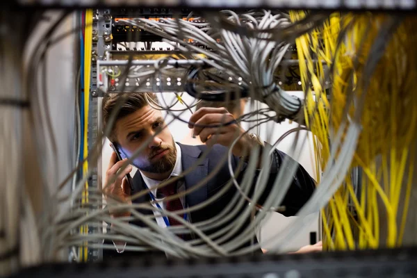 Technician talking on mobile phone while checking cables — Stock Photo, Image