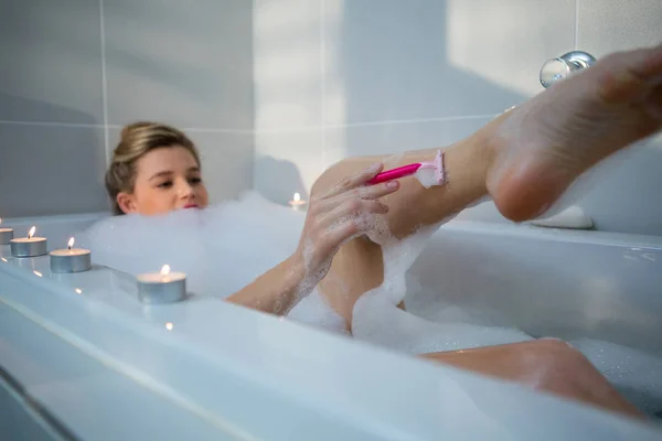 Mujer usando maquinilla de afeitar mientras toma baño —  Fotos de Stock
