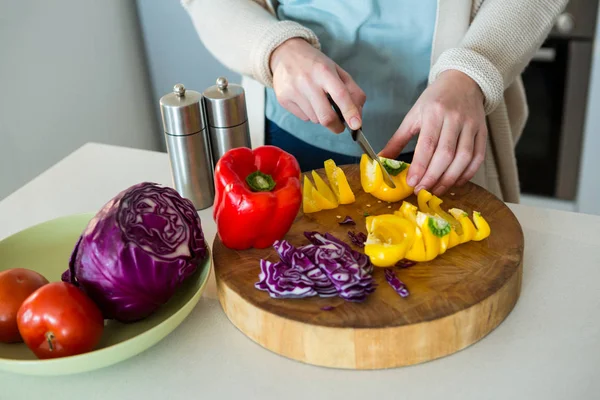 Mulher cortando pimentão amarelo na cozinha — Fotografia de Stock