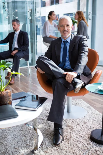 Χαμογελώντας επιχειρηματία που κάθεται σε καρέκλα στο γραφείο — Φωτογραφία Αρχείου