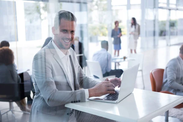 Χαμογελαστός επιχειρηματίας που χρησιμοποιεί φορητό υπολογιστή στο γραφείο — Φωτογραφία Αρχείου