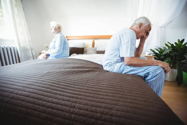 Грустная старшая пара, сидящая на кровати — стоковое фото