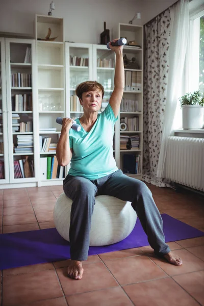 Mulher sênior exercitando com halteres em bola de exercício — Fotografia de Stock