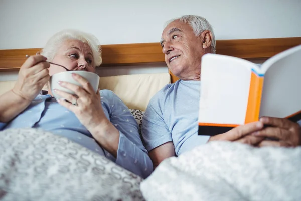 Senior man läsa romanen och kvinna ha frukost — Stockfoto