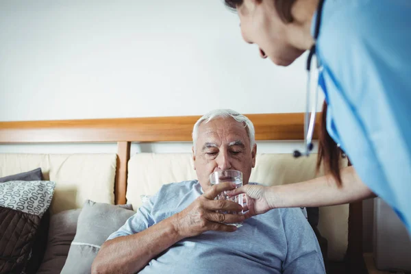 Nurse giving glass of water to senior man — Stock Photo, Image