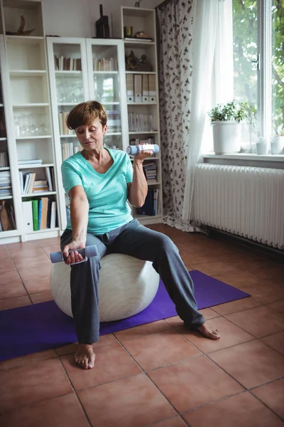 Mulher sênior exercitando com halteres em bola de exercício — Fotografia de Stock
