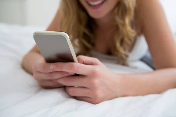 Mulher deitada na cama e usando telefone celular — Fotografia de Stock