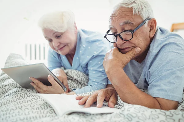 Senior para, czytając książkę i za pomocą tabletu — Zdjęcie stockowe