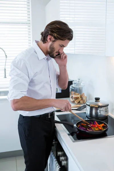 Man talking on mobile phone while preparing food — Stock Photo, Image