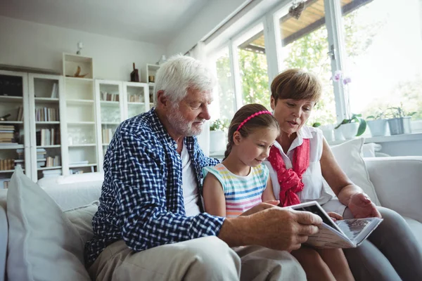 Бабушка с дедушкой и внучка смотрят фотоальбом в гостиной — стоковое фото