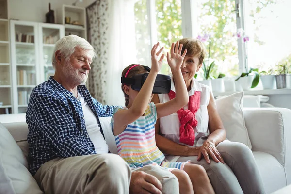 Petite-fille utilisant casque de réalité virtuelle avec ses grands-parents dans le salon — Photo