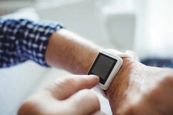 Hombre mayor ajustando un tiempo en smartwatch en sala de estar —  Fotos de Stock