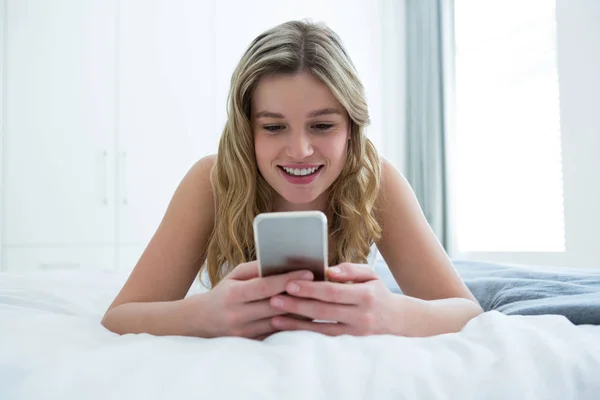 Женщина лежит на кровати и пользуется телефоном — стоковое фото