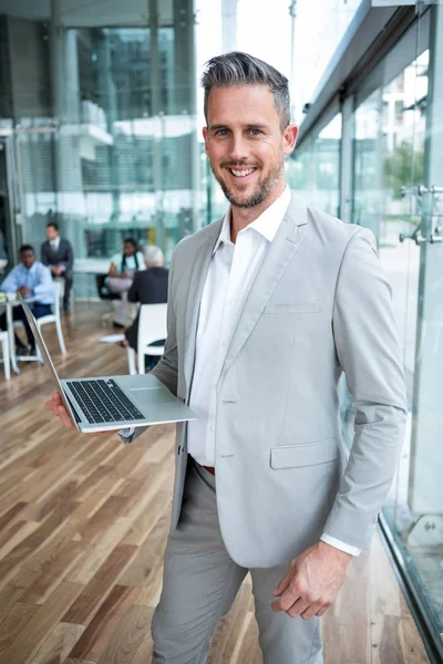 Empresário sorridente segurando laptop no escritório — Fotografia de Stock