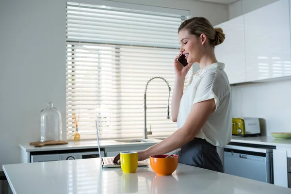 Femme parlant au téléphone tout en utilisant un ordinateur portable — Photo