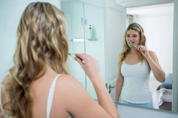 Mujer mirando en el espejo mientras se cepilla los dientes — Foto de Stock
