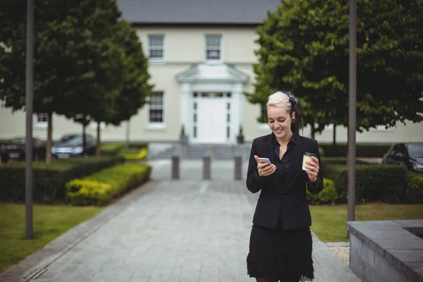 Businesswoman using mobile phone while holding disposable coffee cup — Stock Photo, Image