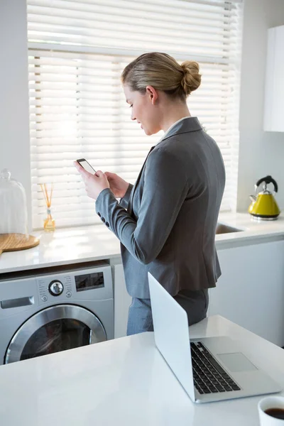 Kobieta przy użyciu telefonu komórkowego w kuchni — Zdjęcie stockowe