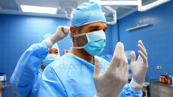 Медсестра помогает хирургу завязать маску — стоковое видео