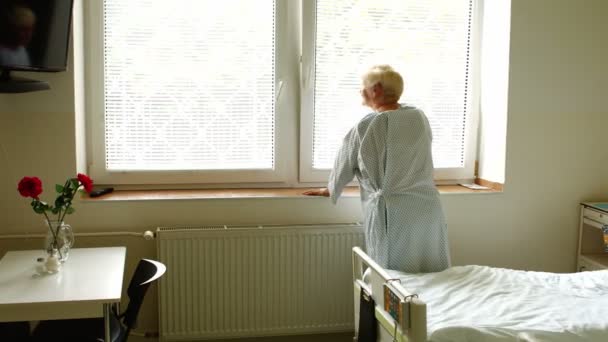 Старшая женщина, стоящая у окна — стоковое видео