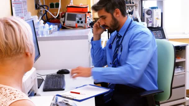 Doctor sentado en el escritorio y hablando por teléfono — Vídeo de stock