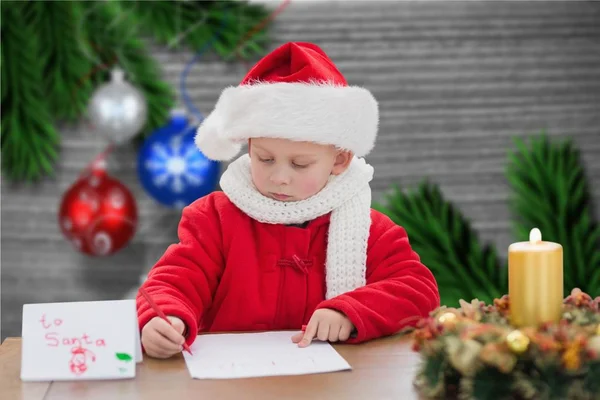 Мальчик в шляпе Санты пишет письмо — стоковое фото
