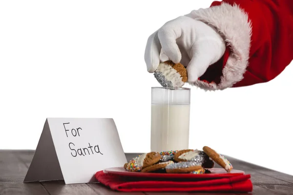 Santa claus dompelen cookies in een glas melk — Stockfoto