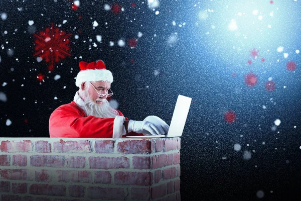 Kerstman met behulp van laptop voor schoorsteen — Stockfoto