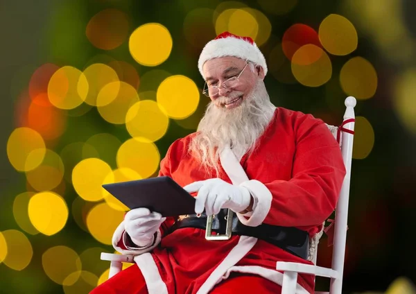 Weihnachtsmann sitzt auf Stuhl und benutzt Tablet — Stockfoto