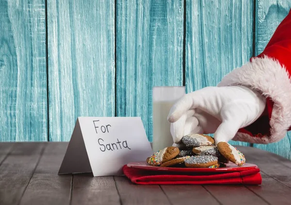 Santa ruka drží cookie na stole — Stock fotografie