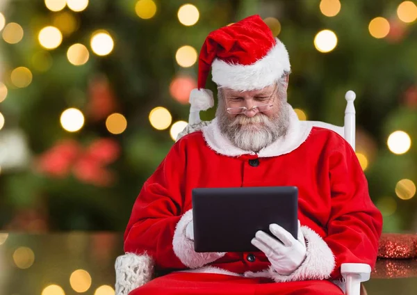 Santa za pomocą tabletu siedząc na krześle — Zdjęcie stockowe