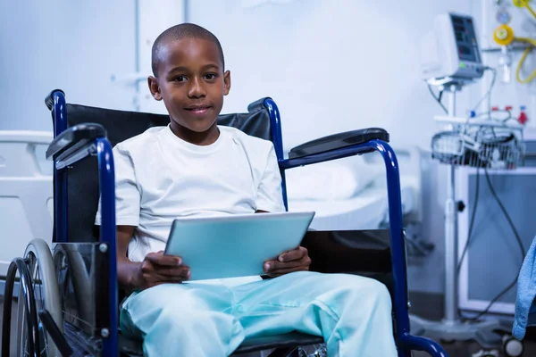 Garçon assis sur fauteuil roulant avec tablette en salle — Photo