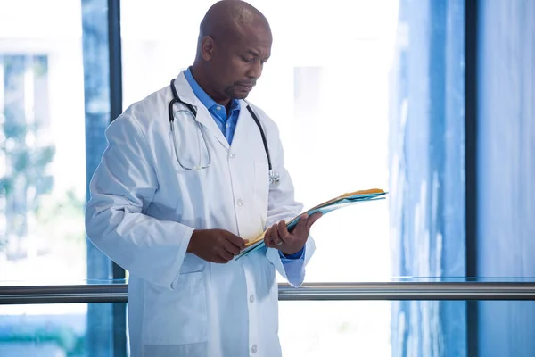 Male doctor reading reports in corridor — Stock Photo, Image