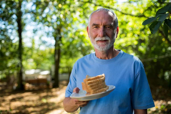 Uomo anziano che tiene fetta di pane in un piatto — Foto Stock