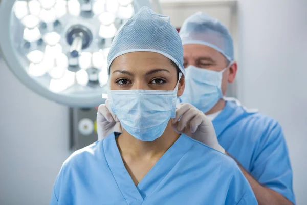 Хирург помогает привязывать хирургическую маску к коллеге — стоковое фото
