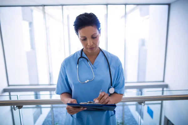 Female nurse writing in clipboard in corridor — Stock Photo, Image