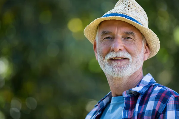 Uomo anziano in cappello in piedi in giardino — Foto Stock