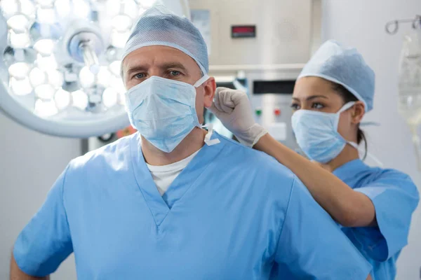 Cirurgião ajudando a amarrar máscara cirúrgica ao colega de trabalho — Fotografia de Stock