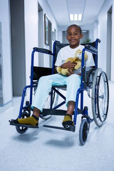 Boy sitting on wheelchair and holding teddy bear — Stock Photo, Image