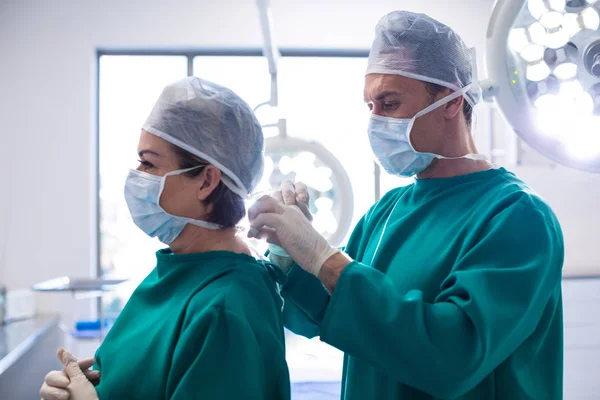 Médico ajudando cirurgião em amarrar máscara cirúrgica — Fotografia de Stock