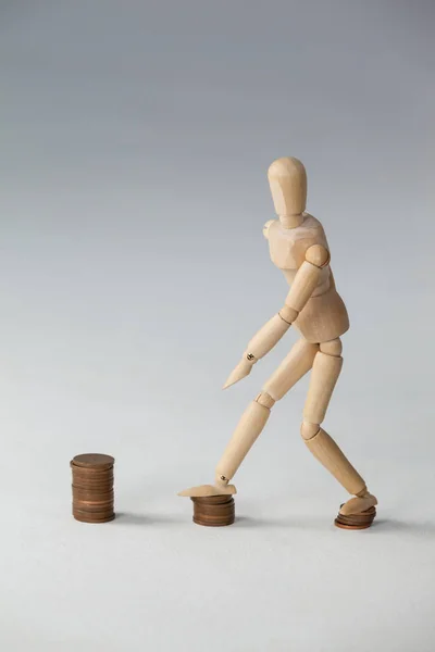 Wooden figurine stepping on stacks of coins — Stock Photo, Image