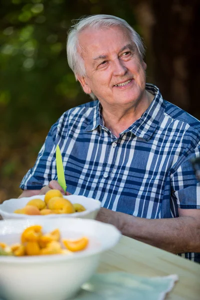 Senior man zit aan tafel met vruchten abrikoos — Stockfoto