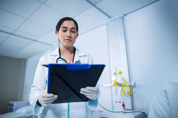 Doctor looking at clipboard in hospital — Stock Photo, Image