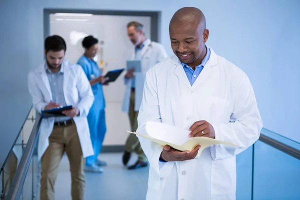 Male doctor reading reports in corridor — Stock Photo, Image
