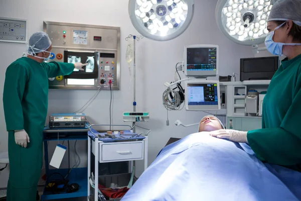 Surgeons discussing x-ray while operating patient — Stock Photo, Image