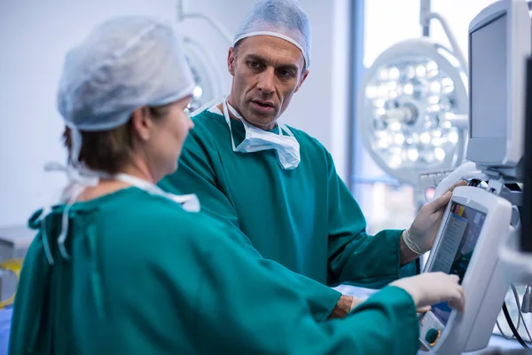 Surgeons discussing a report on surgical monitor — Stock Photo, Image