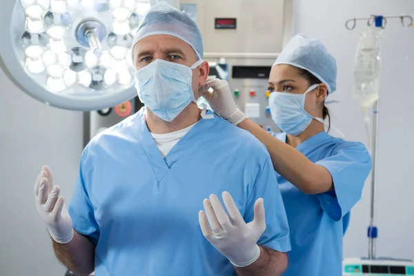Chirurgien aidant à attacher le masque chirurgical à un collègue — Photo