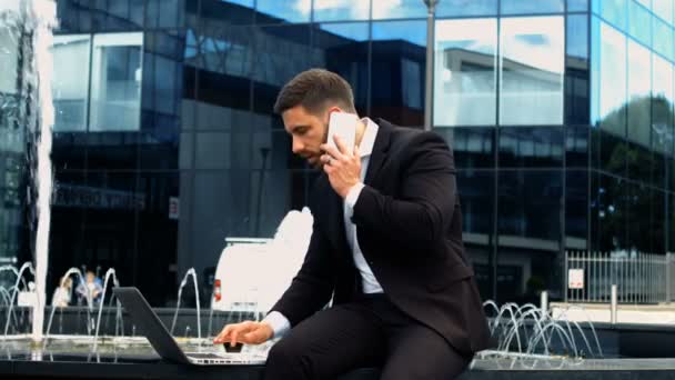 Zakenman met behulp van de laptop tijdens het gesprek op de telefoon — Stockvideo