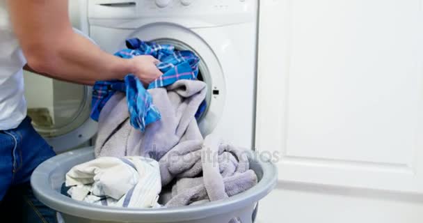 Человек кладет одежду в стиральную машину — стоковое видео